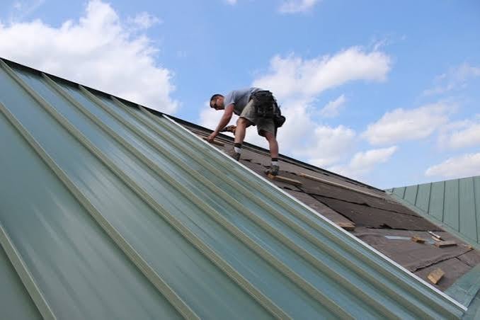 Installer fitting standing-seam metal roofing panels on a sloped roof