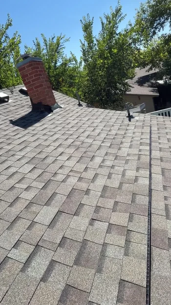 Gray asphalt shingle roof with roof vents and a brick chimney in Windsor, Colorado.